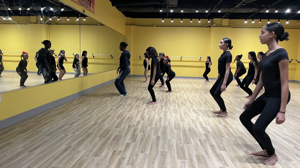 Young dancers face a mirror surrounded by yellow walls at Borinquen Dance Theatre.