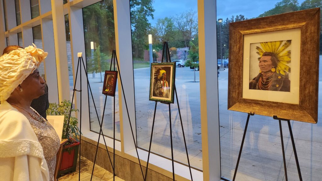 A person in a cream-colored hat looks at art featuring Indigenous people at an event at Nazareth College.