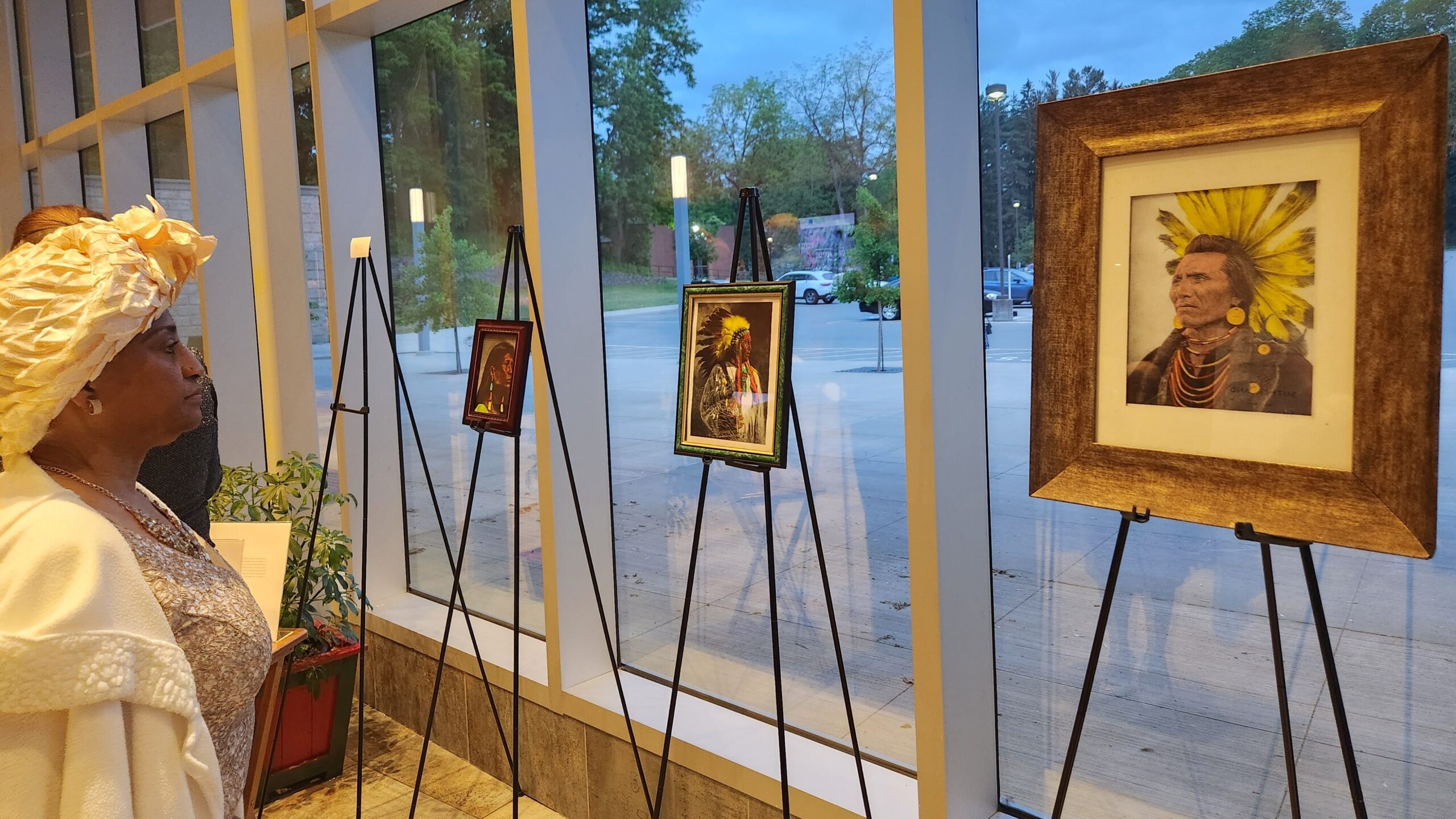 A person in a cream-colored hat looks at art featuring Indigenous people at an event at Nazareth College.