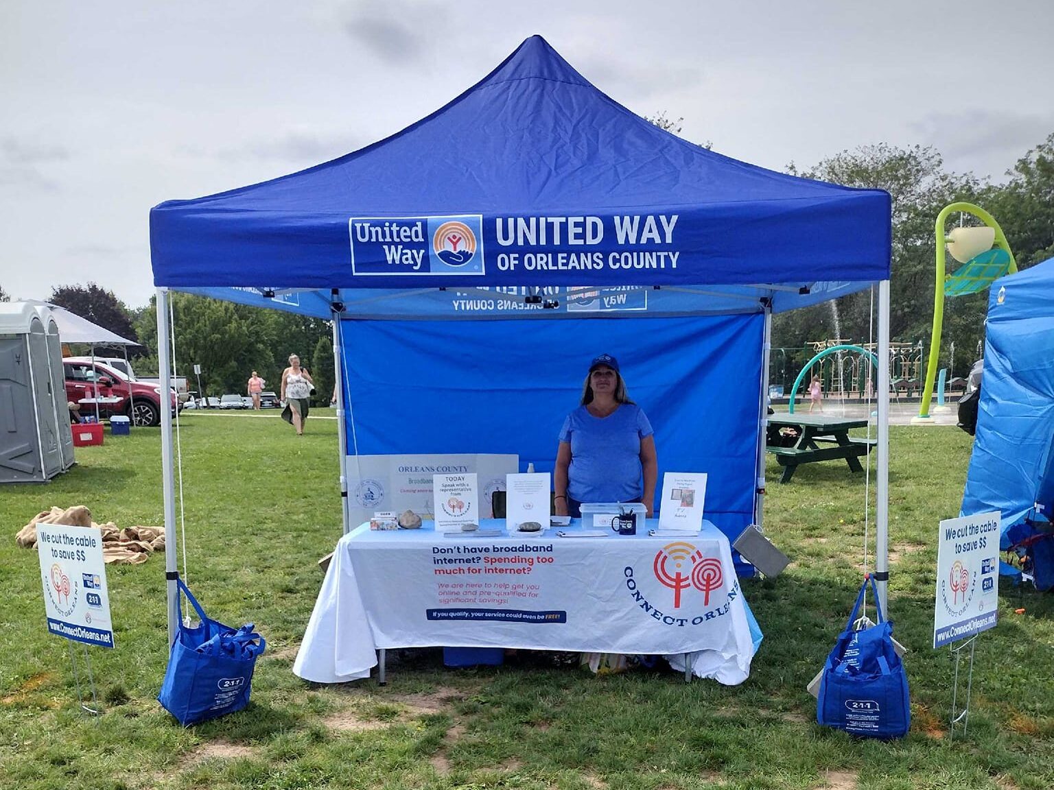 A woman stands under a blue tent outside offering materials on internet access.