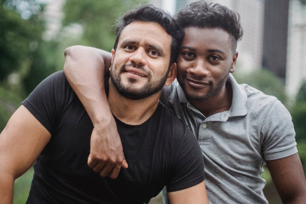 Two men smile at the camera in t-shirts; one man has his arm around the other's shoulder.