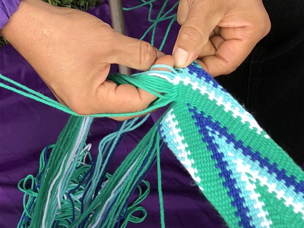 Hands weaving teal and white thread.