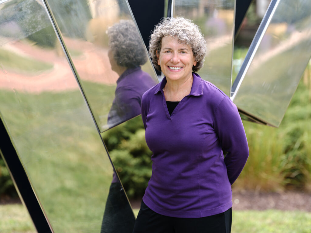 A woman in a purple shirt in front of a mirrored outdoor sculpture