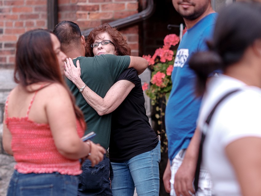 Two people embrace outside of a brick building.