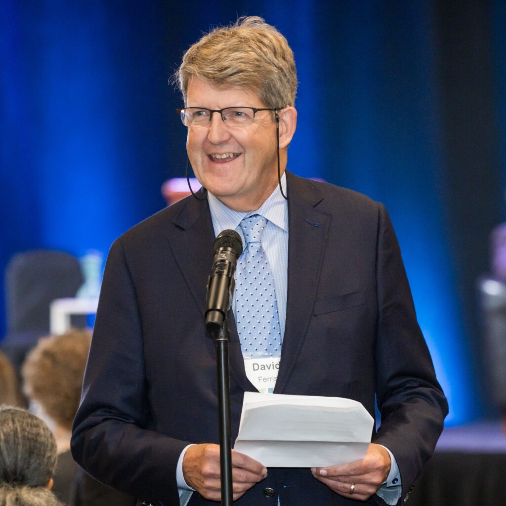 A man wearing glasses holds a piece of paper standing in front of a microphone.