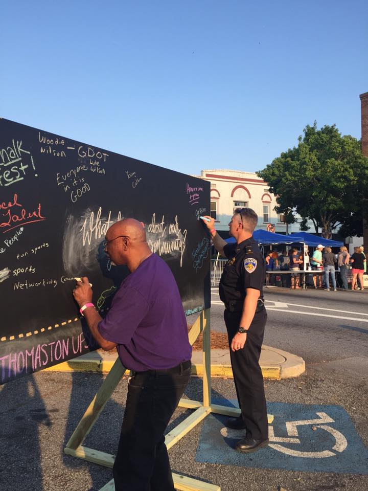Two men write on a large chalkboard outdoors