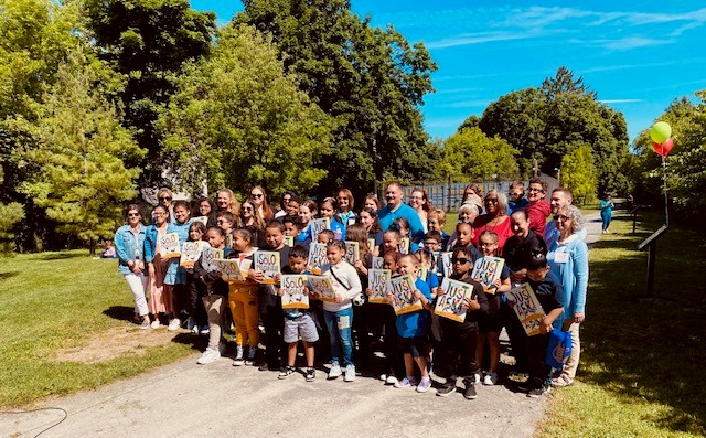 A large group of children outside holding copies of a book in English and Spanish.