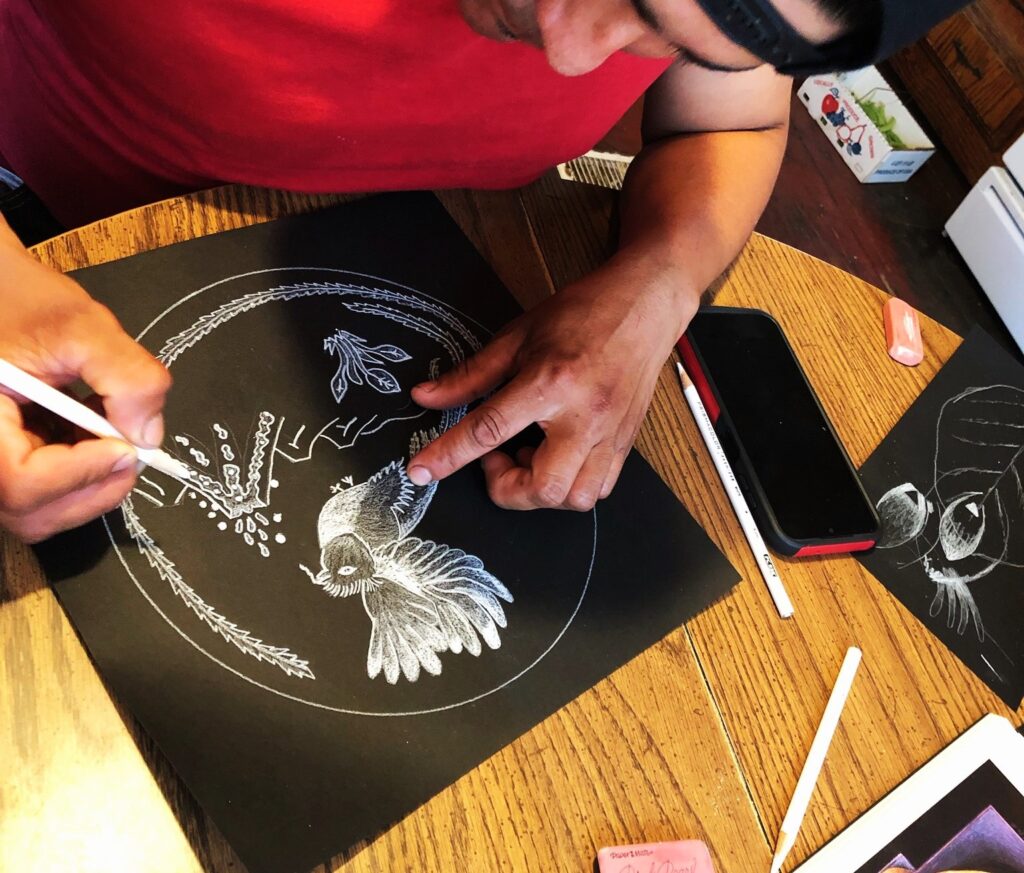 A person drawing a bird with while pencil on black paper