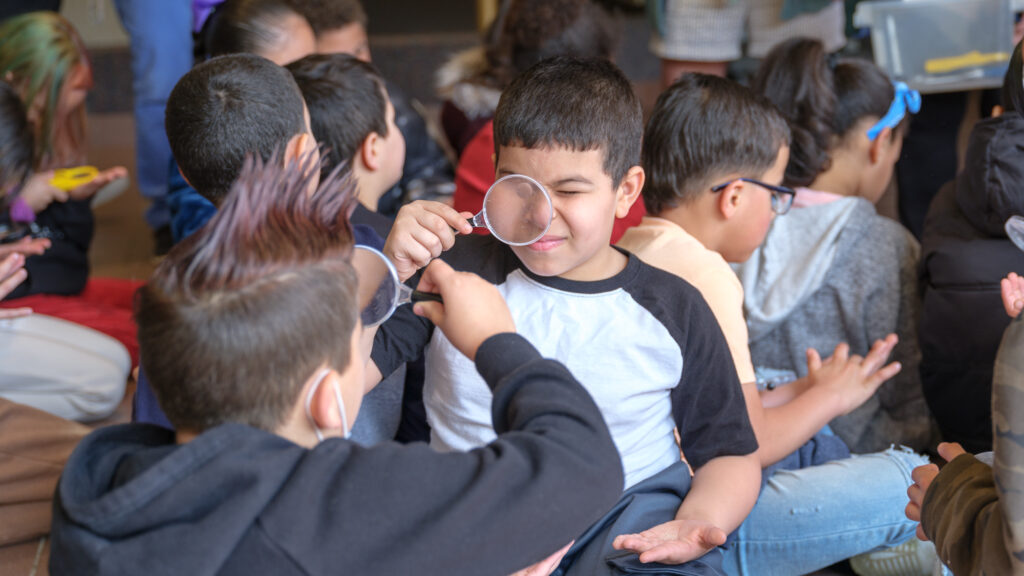 Two young kids look at each other through hand microscopes