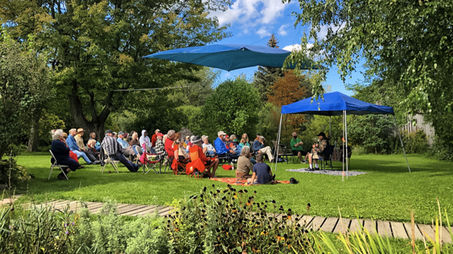 A crowd gathers on chairs on a green lawn