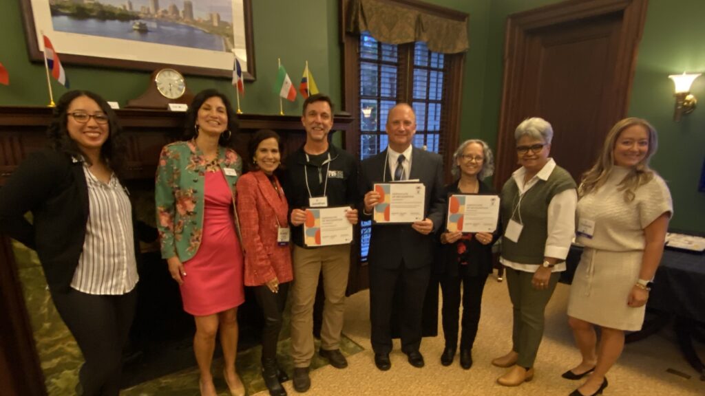 Eight people pose in a line wearing formal clothes, three of them hold grant award certificates