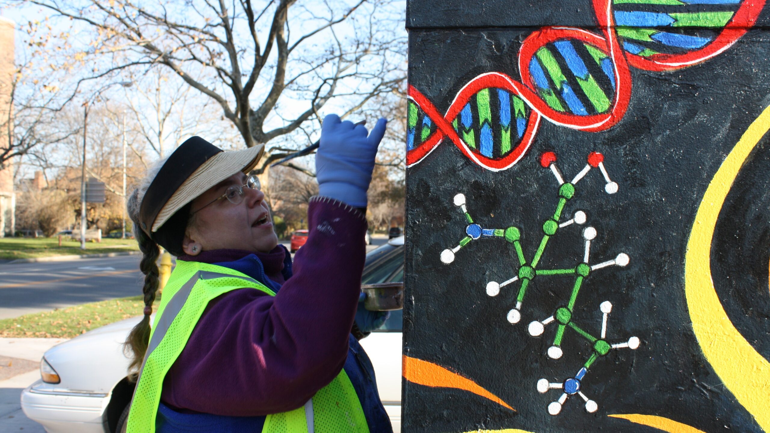 Someone painting an electric box with drawings of DNA