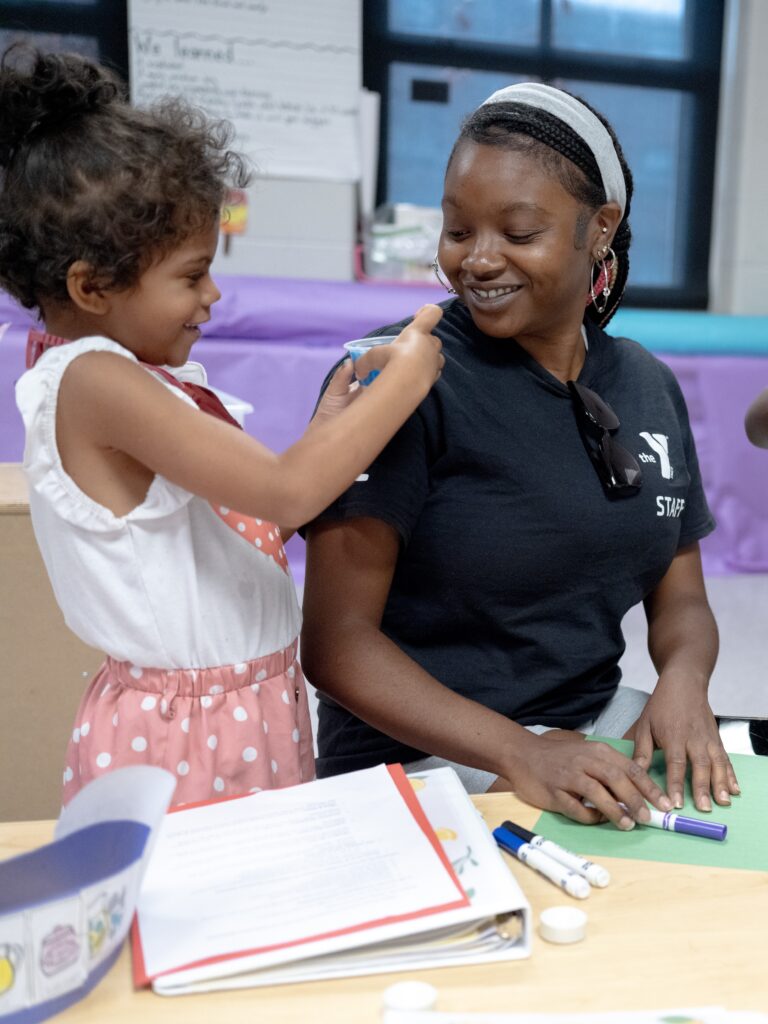 A young girl and an older camp staff member do an activity at a table