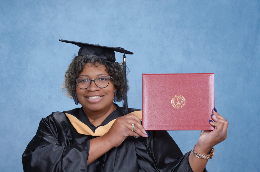 A woman in a graduation cap and gown holding her diploma.