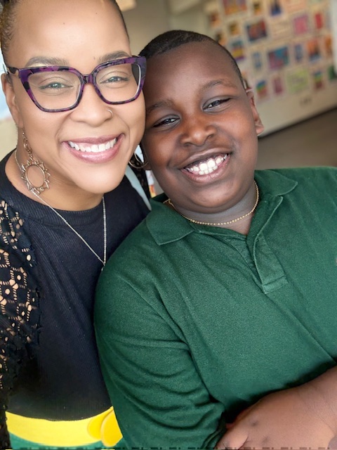 A woman in purple glasses smiles with her son in a green shirt.