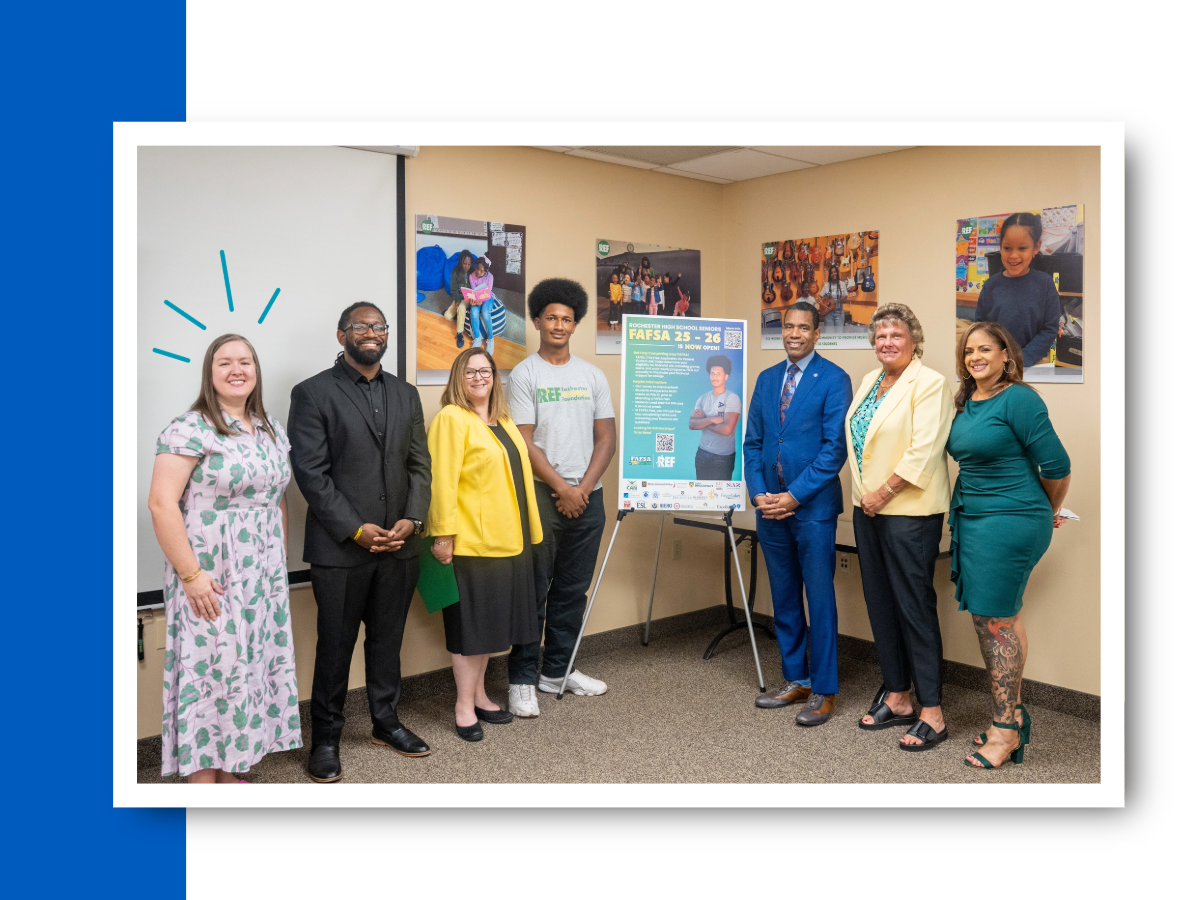 A woman in a purple and green dress stands next to others - including the mayor - around a FAFSA poster.