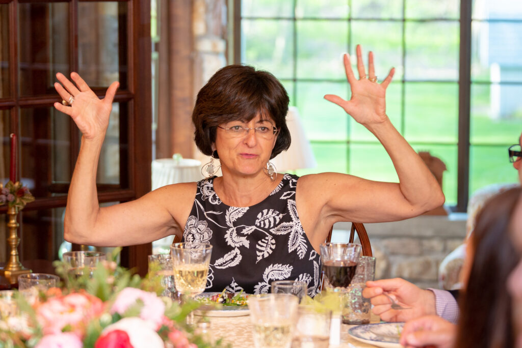 A woman raises both hands in the air at a dinner table.