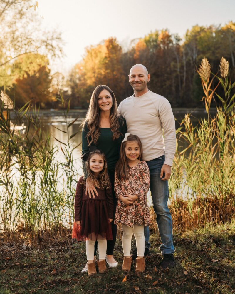 A woman in a green shirt stands next to a man and two young girls in front of a pond