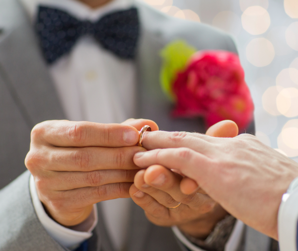 A man in a tuxedo puts a ring on another man's finger.