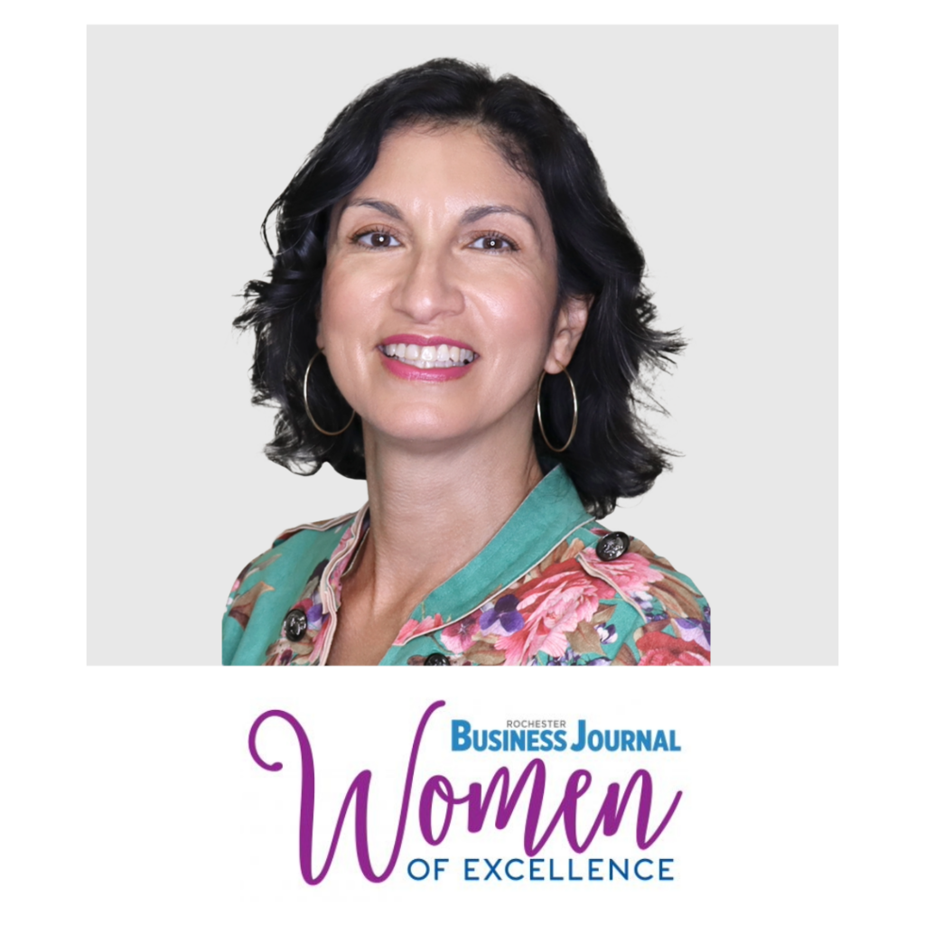 Rochester Business Journal Women of Excellence. A woman in silver hoops earrings and a teel and pink floral jacket.