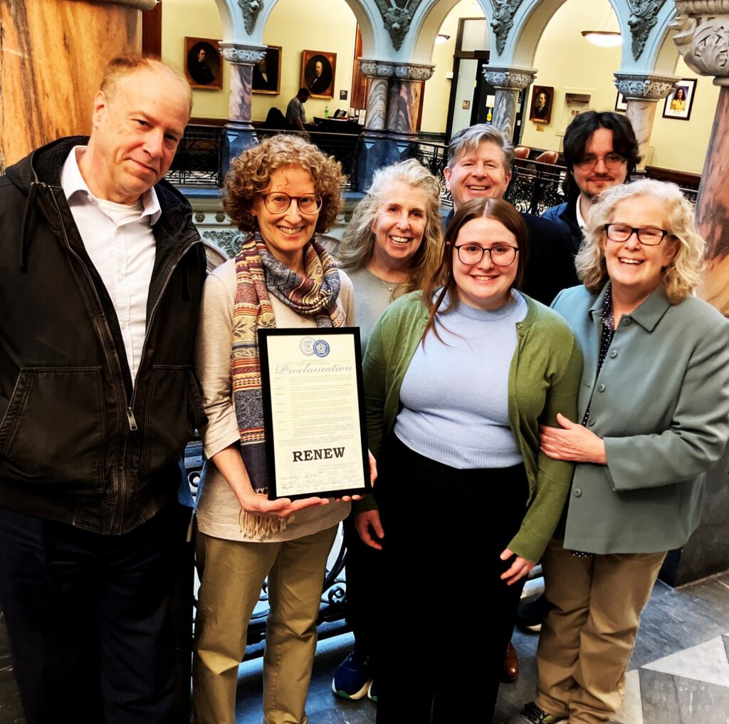 A group of people in a government building holding a Rochester City Council proclamation and smiling.