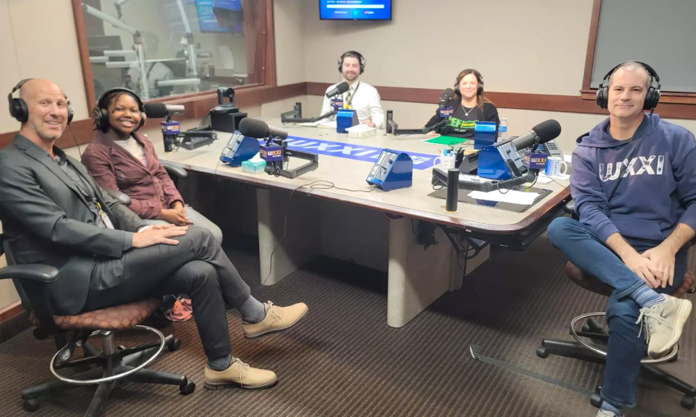 Five people sit around a table with microphones in a WXXI studio.