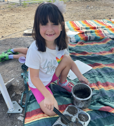 A young girl on a striped blanket creates compost in muffin tins.