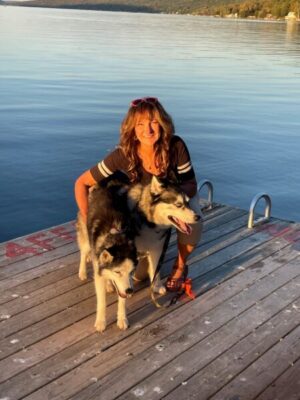 A person with a dog on a dock next water.