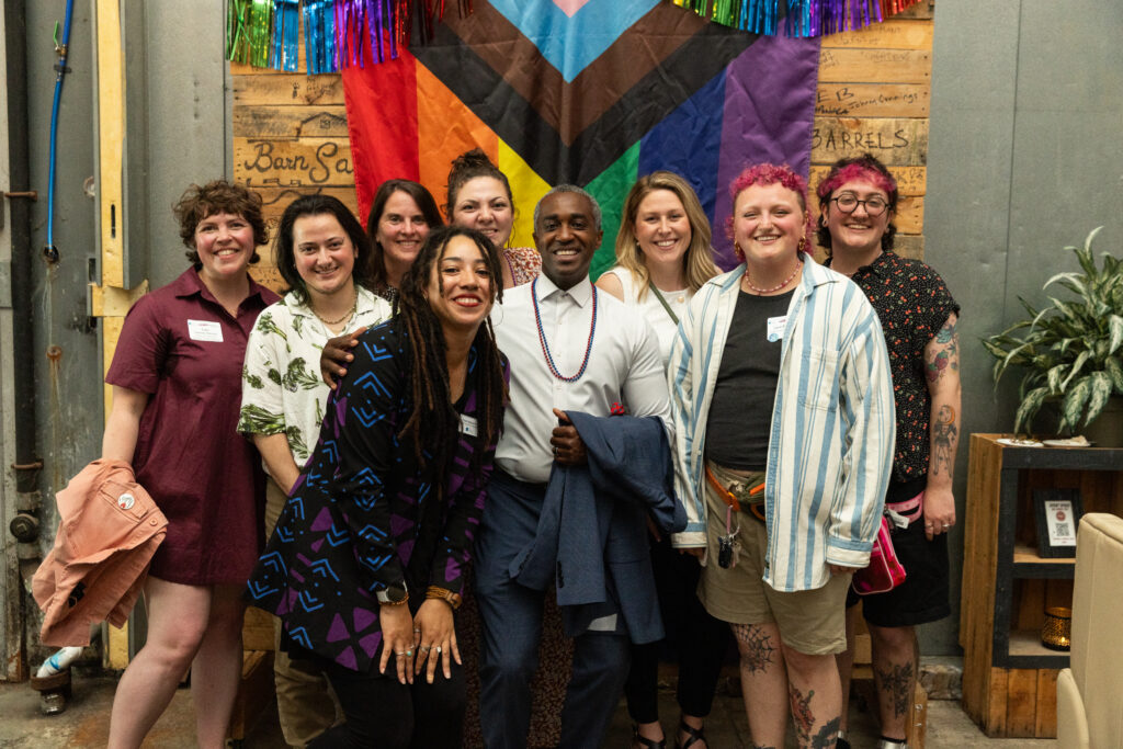 Nine people smiling in front of a pride flag