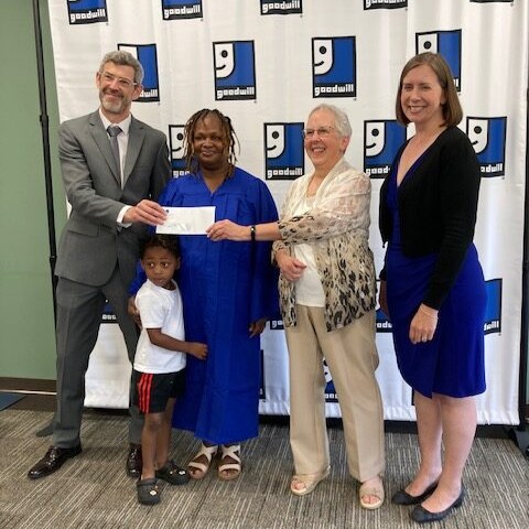 People smiling in front of a Goodwill banner with an envelope.