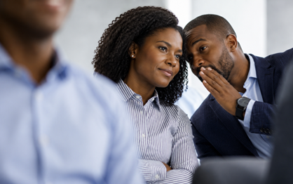 A man in a suit whispering to a woman in a blue blouse.